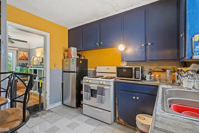 kitchen with appliances with stainless steel finishes, sink, a textured ceiling, and blue cabinetry