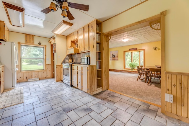 kitchen featuring appliances with stainless steel finishes, light colored carpet, light brown cabinets, wood walls, and ceiling fan