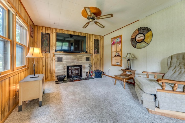 carpeted living room featuring a fireplace, a wood stove, wood walls, and ceiling fan