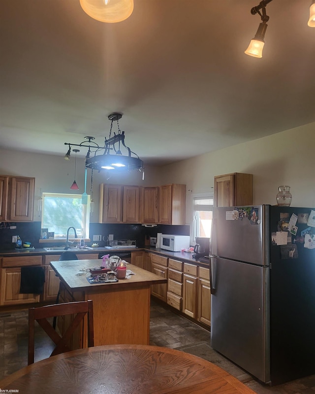 kitchen with pendant lighting, stainless steel fridge, sink, backsplash, and a center island