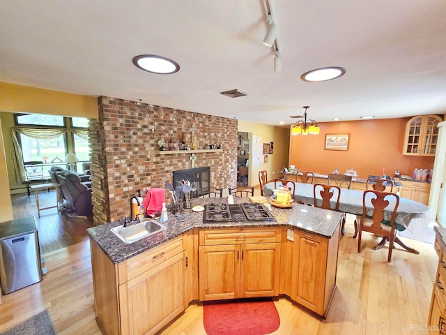 kitchen featuring light hardwood / wood-style flooring, dark stone countertops, sink, and a brick fireplace