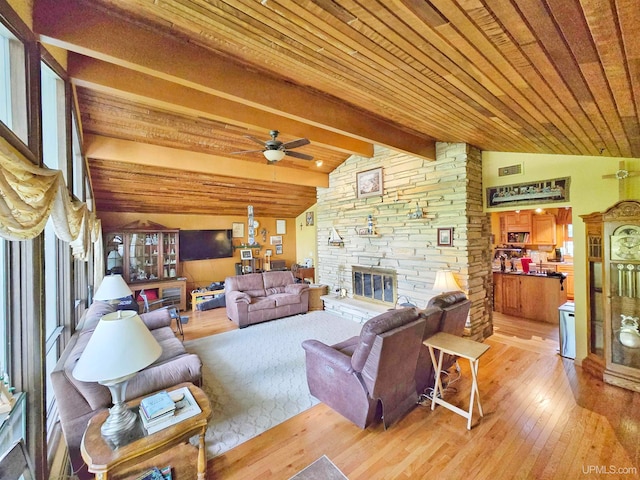 living room featuring a stone fireplace, wood-type flooring, lofted ceiling with beams, plenty of natural light, and ceiling fan