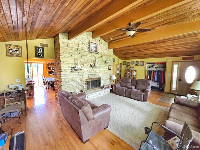 living room with ceiling fan, hardwood / wood-style floors, a stone fireplace, and vaulted ceiling with beams