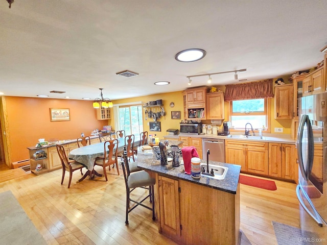 kitchen featuring stainless steel appliances, light hardwood / wood-style floors, sink, a baseboard radiator, and a breakfast bar