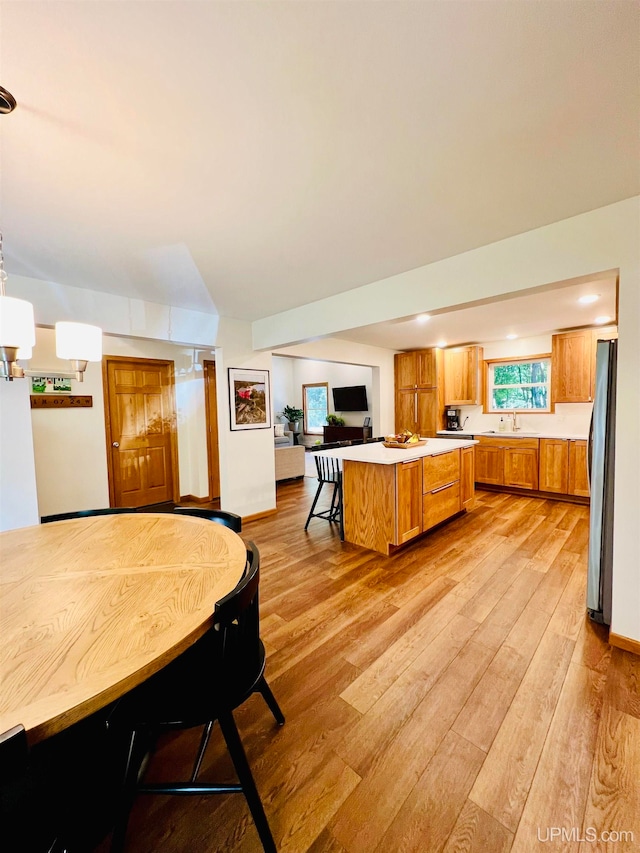 kitchen with light hardwood / wood-style flooring, sink, stainless steel refrigerator, and a kitchen breakfast bar