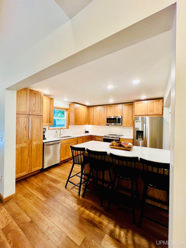 kitchen featuring appliances with stainless steel finishes, hardwood / wood-style flooring, a breakfast bar area, and sink