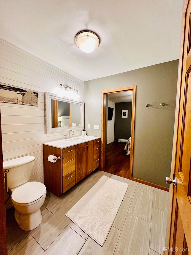 bathroom featuring wood walls, wood-type flooring, toilet, and vanity