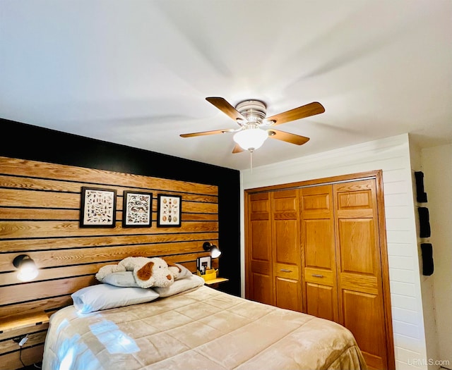 bedroom with ceiling fan, wood walls, and a closet