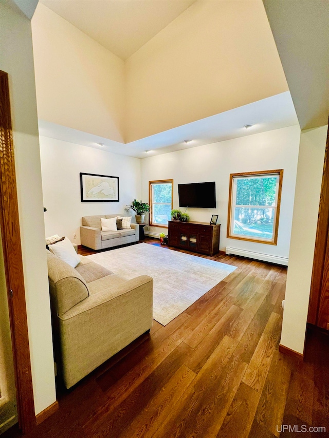 living room with a baseboard heating unit, dark wood-type flooring, and a towering ceiling