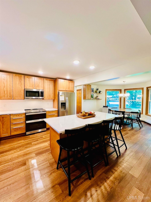 kitchen featuring light hardwood / wood-style flooring, appliances with stainless steel finishes, a kitchen bar, hanging light fixtures, and a chandelier