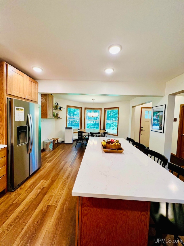 kitchen featuring hardwood / wood-style floors, a kitchen bar, decorative light fixtures, a center island, and stainless steel fridge with ice dispenser