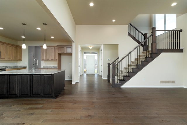 kitchen with dark wood-type flooring, sink, light stone countertops, and a kitchen island with sink