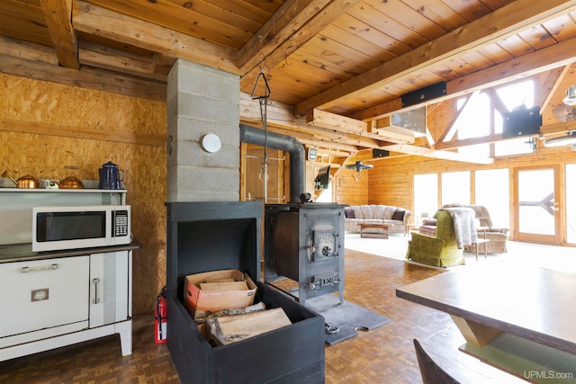 living room with a wood stove, a healthy amount of sunlight, beam ceiling, and wooden walls