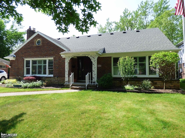 view of front facade with a shingled roof, a front yard, brick siding, and a chimney