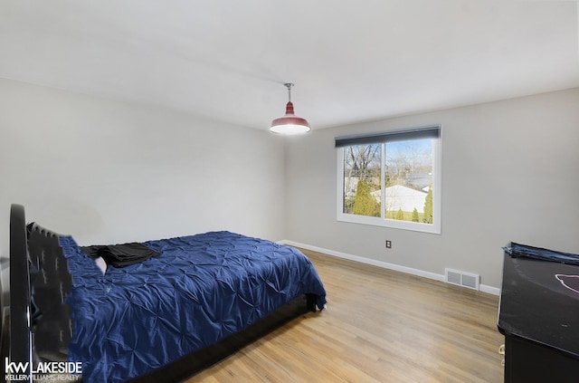 bedroom with baseboards, visible vents, and wood finished floors