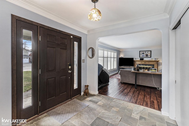 foyer entrance with arched walkways, crown molding, baseboards, and stone tile floors