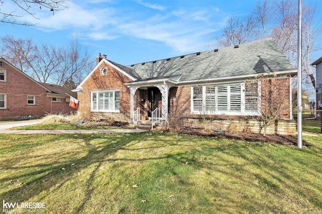 view of front of house featuring a front lawn, roof with shingles, a chimney, and brick siding