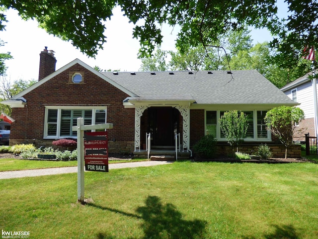 view of front of home featuring brick siding, a chimney, a front yard, and a shingled roof