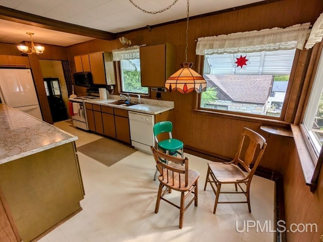 kitchen featuring white appliances, wood walls, sink, and hanging light fixtures