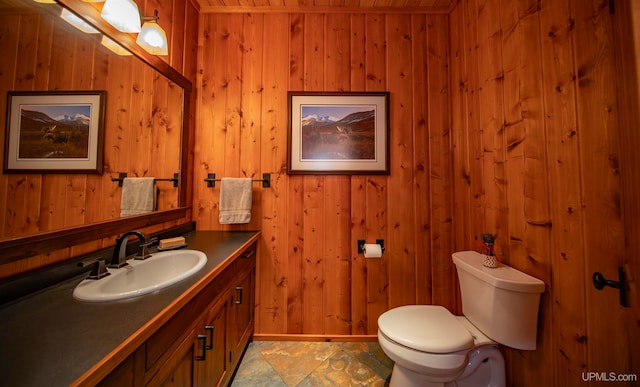 bathroom featuring vanity, toilet, and wooden walls