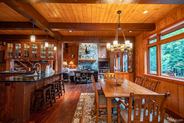 dining space featuring dark wood-type flooring, wooden walls, and beam ceiling