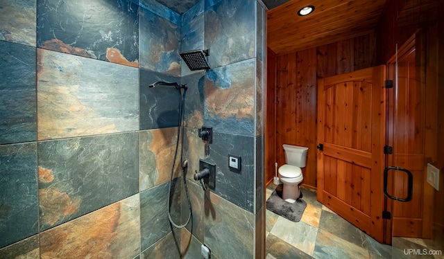 bathroom with tiled shower, toilet, and wood walls