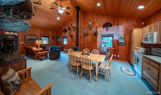 carpeted dining space with lofted ceiling, ceiling fan, a wood stove, and wooden walls