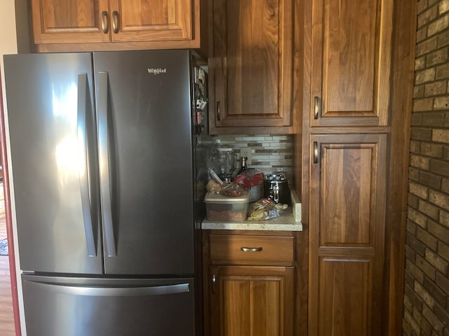 kitchen featuring tasteful backsplash, stainless steel refrigerator, and brick wall