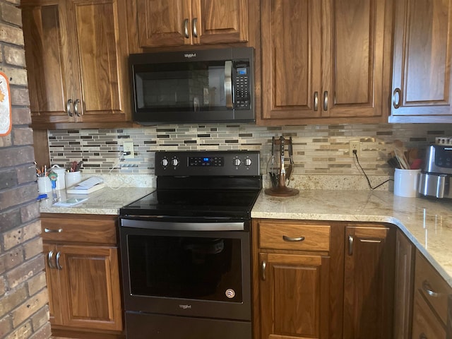 kitchen featuring backsplash, light stone countertops, stainless steel appliances, and brick wall