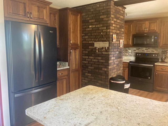 kitchen with a textured ceiling, stainless steel appliances, light stone countertops, and light hardwood / wood-style floors