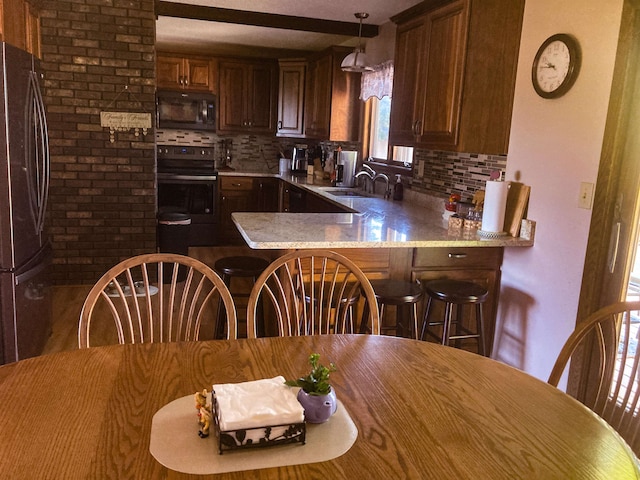 kitchen with decorative light fixtures, sink, black appliances, kitchen peninsula, and tasteful backsplash