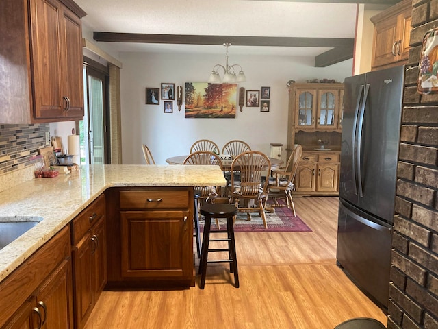 kitchen featuring backsplash, light hardwood / wood-style floors, kitchen peninsula, black fridge, and a kitchen bar