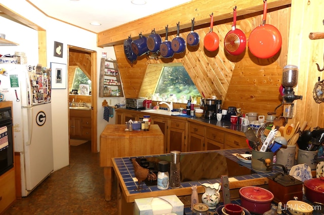 kitchen featuring beamed ceiling, a sink, freestanding refrigerator, tile countertops, and wood walls