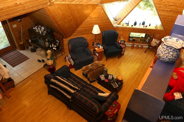 living area featuring vaulted ceiling with skylight, baseboard heating, wood walls, and wood finished floors