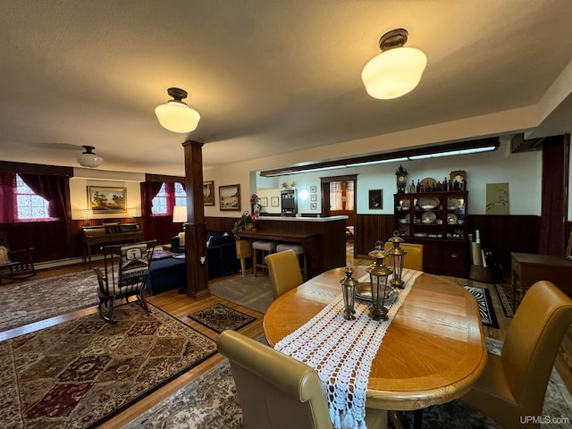 dining area with hardwood / wood-style floors, wood walls, and ornate columns