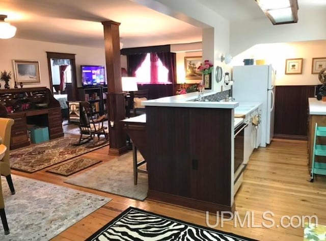 kitchen with light hardwood / wood-style flooring, kitchen peninsula, white fridge, a breakfast bar area, and dark brown cabinets