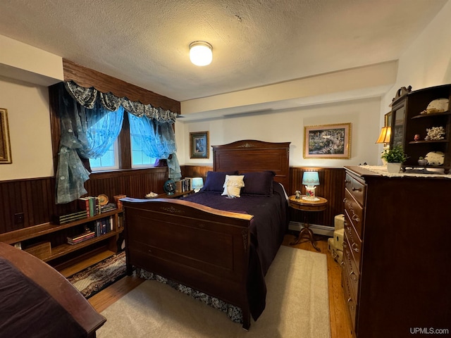 bedroom with light hardwood / wood-style flooring, wood walls, a textured ceiling, and a baseboard radiator