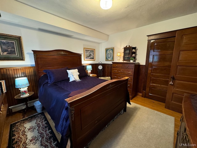 bedroom featuring light hardwood / wood-style floors, a textured ceiling, wooden walls, and a baseboard heating unit