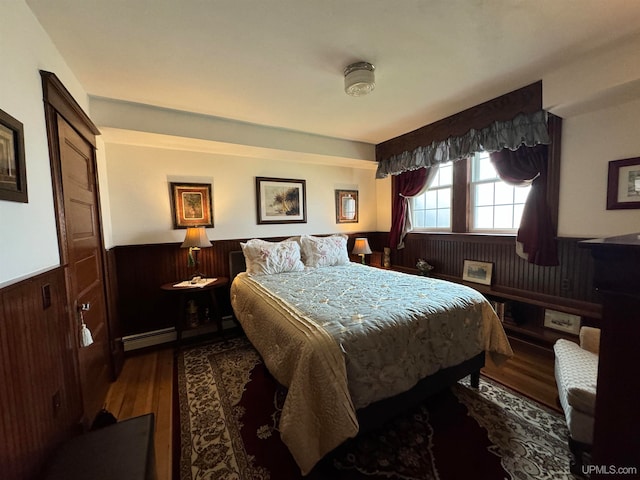 bedroom with hardwood / wood-style floors, wooden walls, and a baseboard heating unit