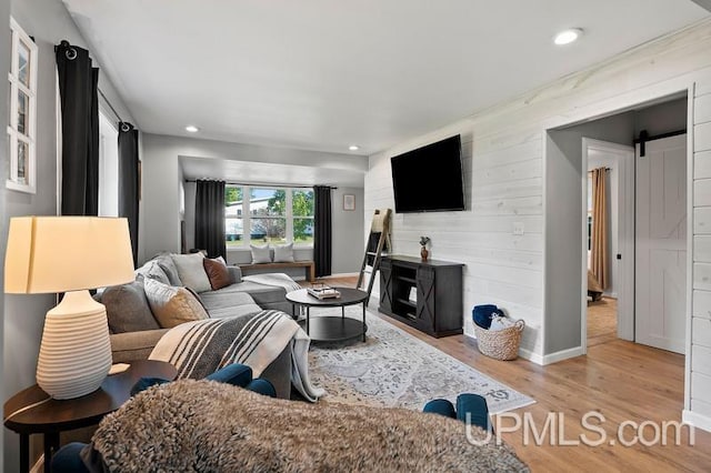 living room with a barn door, light wood-type flooring, and wooden walls