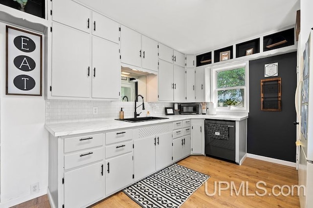 kitchen with black appliances, sink, white cabinetry, and light hardwood / wood-style floors