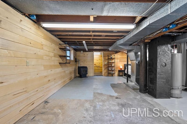 basement with gas water heater, wood walls, and a wood stove