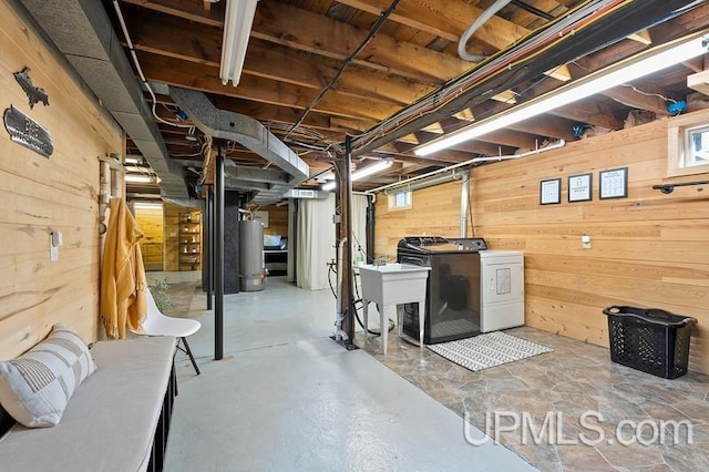 basement featuring washer and dryer, wood walls, sink, and water heater