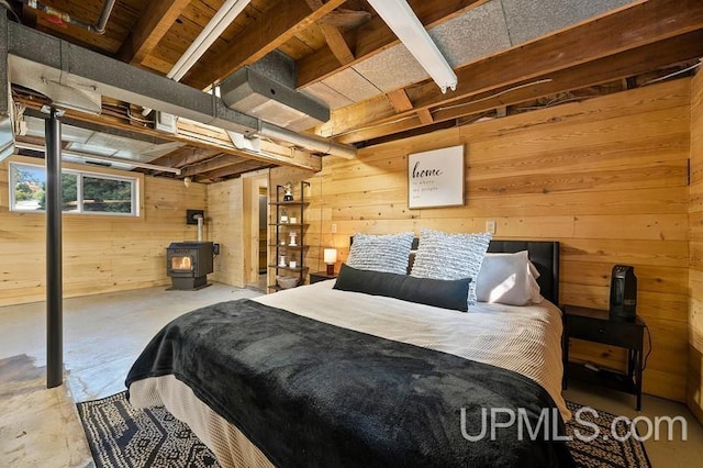 bedroom featuring a wood stove, wooden walls, and concrete flooring