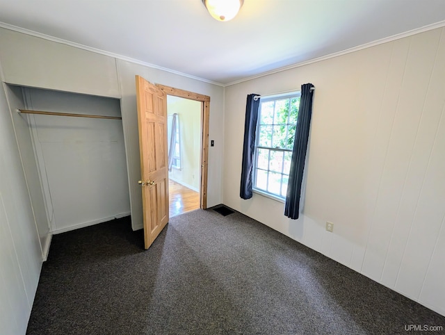 unfurnished bedroom featuring crown molding, dark carpet, and a closet