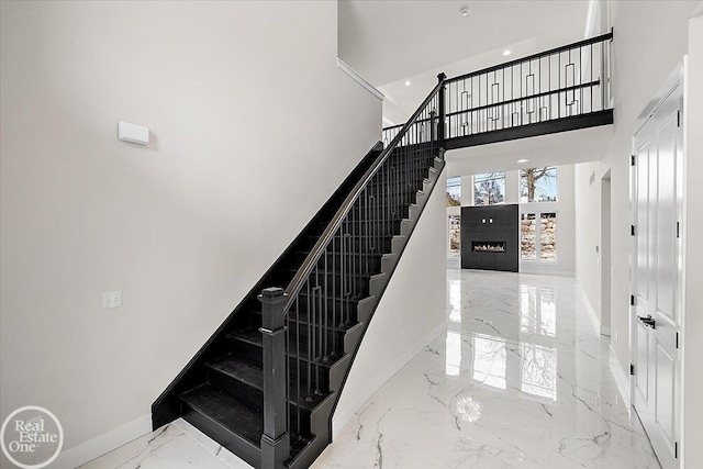 stairs featuring baseboards, recessed lighting, a fireplace, a high ceiling, and marble finish floor