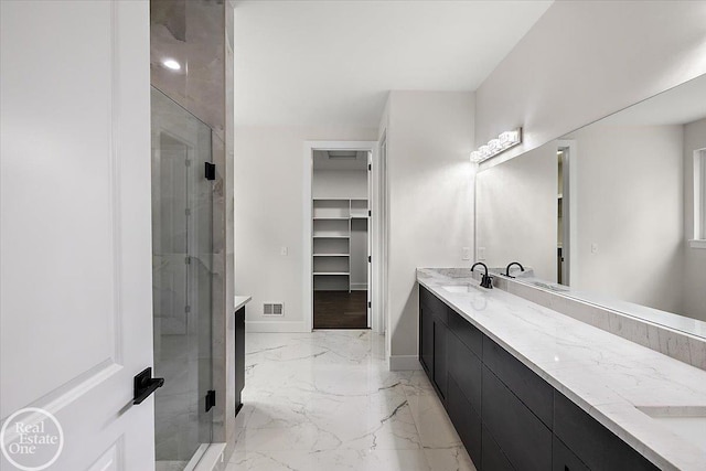 full bath with a sink, marble finish floor, a spacious closet, a shower stall, and double vanity