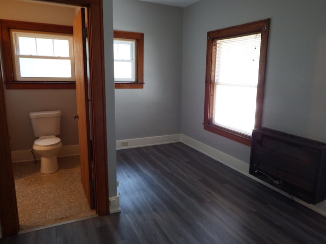 unfurnished bedroom with heating unit, multiple windows, and dark wood-type flooring