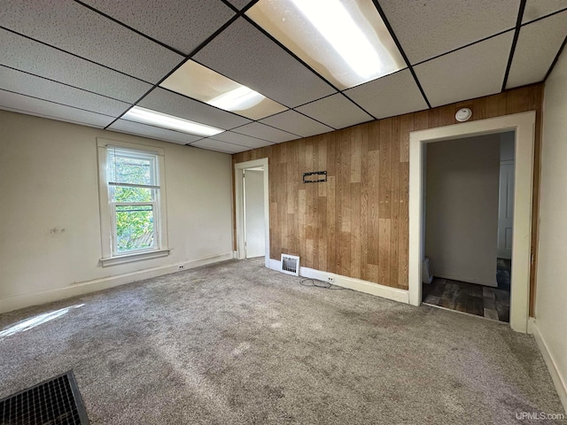 carpeted spare room featuring a paneled ceiling and wooden walls