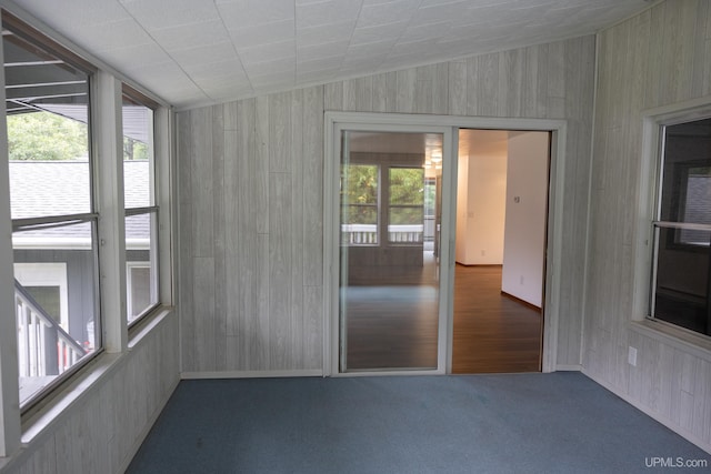 interior space with lofted ceiling, a wealth of natural light, wooden walls, and carpet